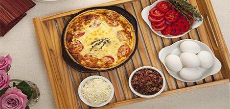 Black iron skillet filled with a breakfast quiche with sliced tomatoes and bacon bits