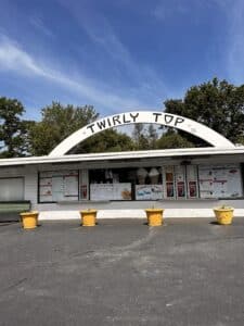 Twirly Top Ice Cream is an outdoor ice cream shop with four yellow planters in front of it, trees and a blue sky on top. 