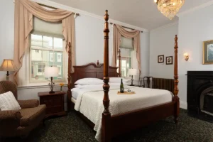 Ewing Room has a four poster king bed. A cozy chair sits in the corner and an antique fireplace in the other
