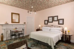 Rose room has a king metal bed framed bed. A Bistro table sits on the side and 4 flower drawings hang above the bed.