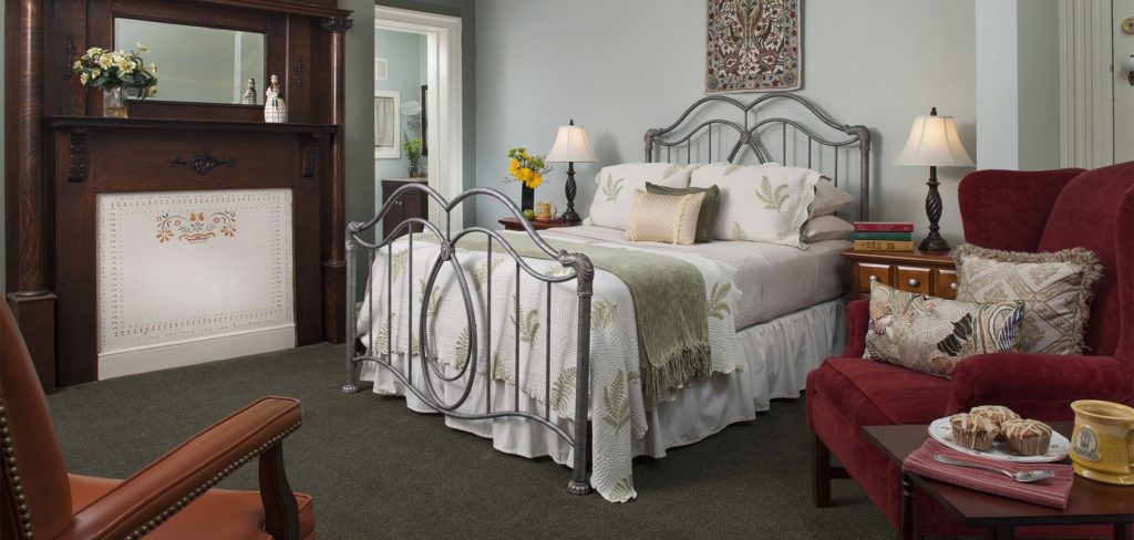 Seren and spacious carpeted guest room and bed topped with white and sage green bedding