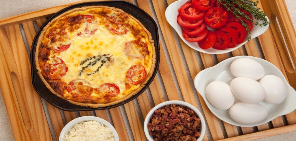 Tray topped with baked quiche, red tomatoes, crumbly bacon and shredded cheese