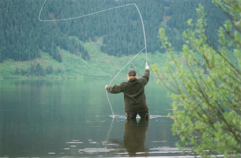 Person fly fishing in a body of water surrounded by green trees